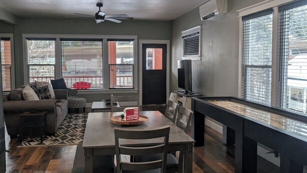 A spacious living room with a dining area, a pool table, and a ceiling fan. There are large windows with blinds and an air conditioning unit on the wall. - Cozy, remodeled townhome retreat in downtown Historic Wallace! (Wallace)