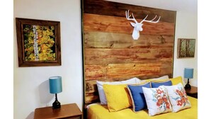 Une chambre à coucher avec une tête de lit en bois, un lit avec une literie jaune et des coussins à motifs floraux, une table de chevet avec une lampe et un tableau encadré au mur.