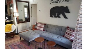 Un salon avec un canapé d’angle gris, deux tabourets ronds, un miroir et une silhouette d’ours fixée au mur.
