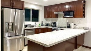 A modern kitchen with stainless steel appliances, wooden cabinets, and a large island. - CONDO T  BY TRVL2HM (Nuevo Nayarit)