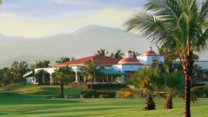 A golf course with a clubhouse featuring domed roofs and a mountainous backdrop. - CONDO T  BY TRVL2HM (Nuevo Nayarit)