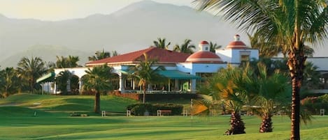 A golf course with a clubhouse featuring domed roofs and a mountainous backdrop.