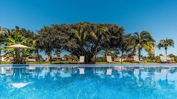 A clear blue pool with tiled edges, surrounded by palm trees and lounge chairs. - CONDO T  BY TRVL2HM (Nuevo Nayarit)