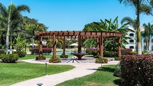A garden area with a pergola, palm trees, and a pool. - CONDO T  BY TRVL2HM (Nuevo Nayarit)