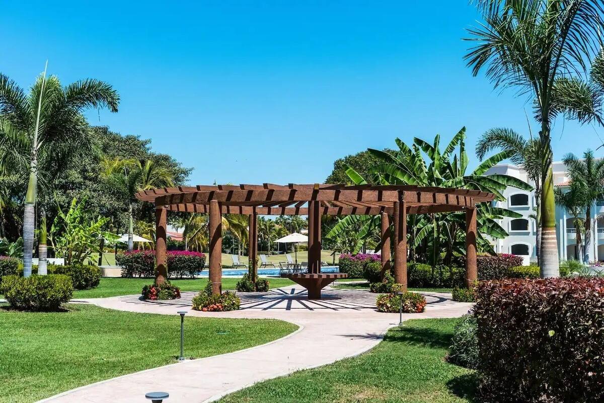 A garden area with a pergola, palm trees, and a pool.