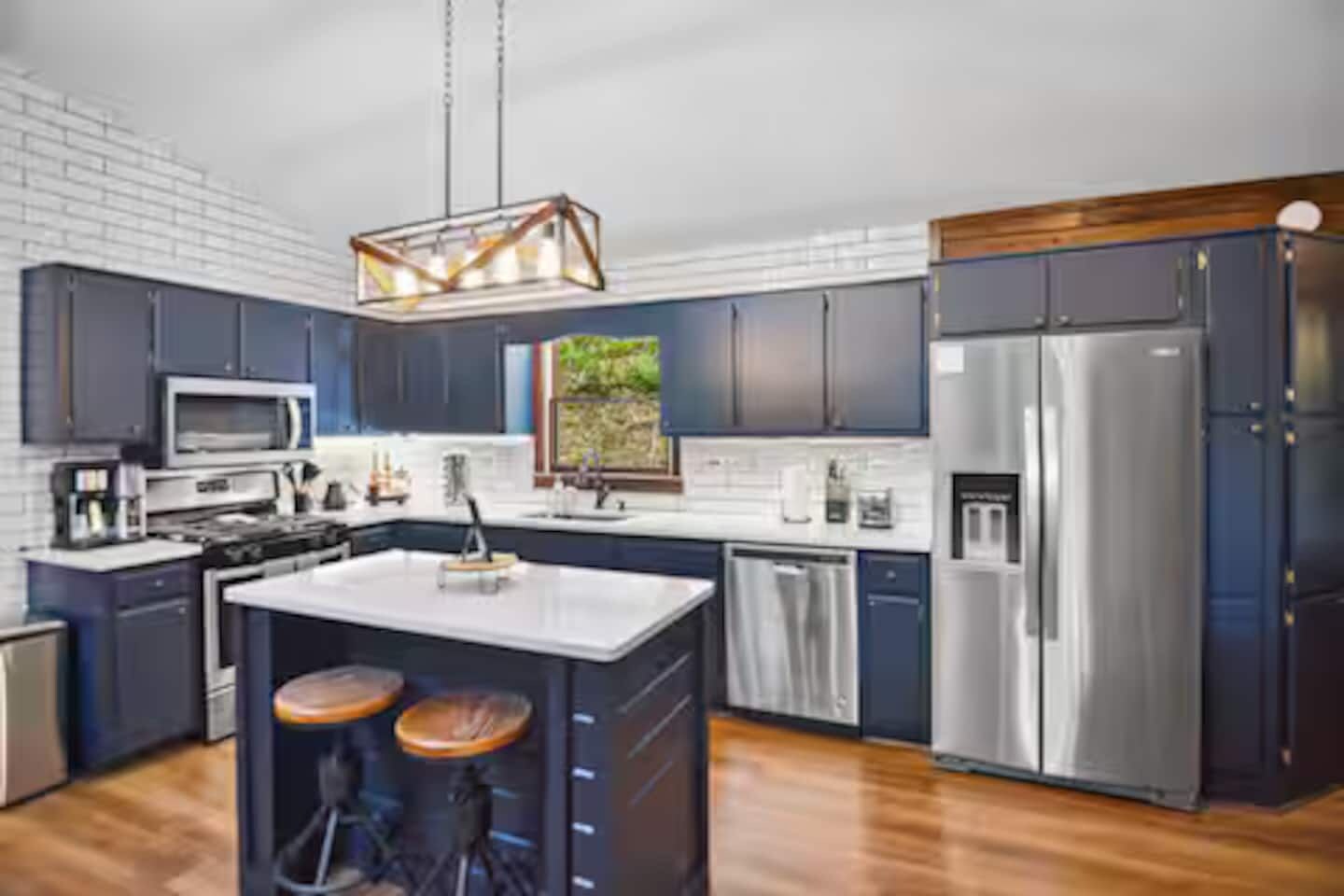 A modern kitchen with dark cabinetry, stainless steel appliances, and a central island with stools.