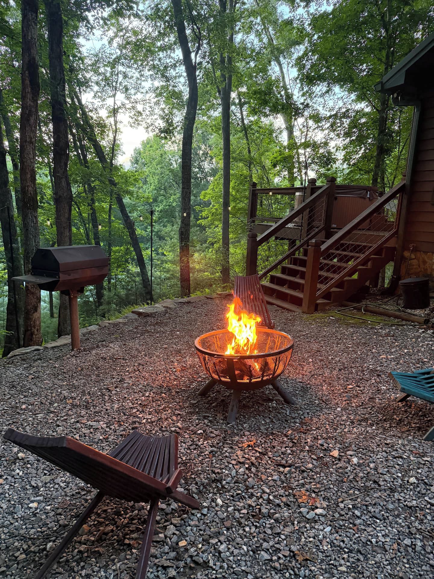 A fire pit in a forested area with a wooden deck and a mailbox.