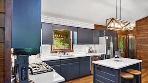Une cuisine moderne avec des meubles de couleur sombre, un plan de travail blanc et un îlot central intégré avec des tabourets.