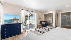 Ein Schlafzimmer mit Bett, Kommode, Fernseher, Sessel, kleinem Tisch und einer Tür, die auf einen Balkon führt.