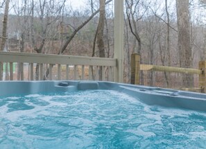 Ein Whirlpool mit einer Holzterrasse und Blick auf Bäume ohne Blätter im Hintergrund.