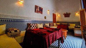 A traditional Moroccan room with a checkered floor, patterned walls, and a bed with a red bedspread. - Suite Avec 4lits Dans un Riad Luxueuse a fes (fes)