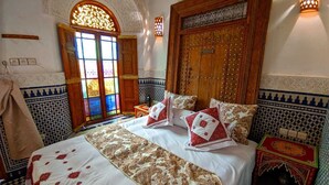 A traditional room with a large bed, ornate wooden door, and patterned walls. - Suite Avec 4lits Dans un Riad Luxueuse a fes (fes)