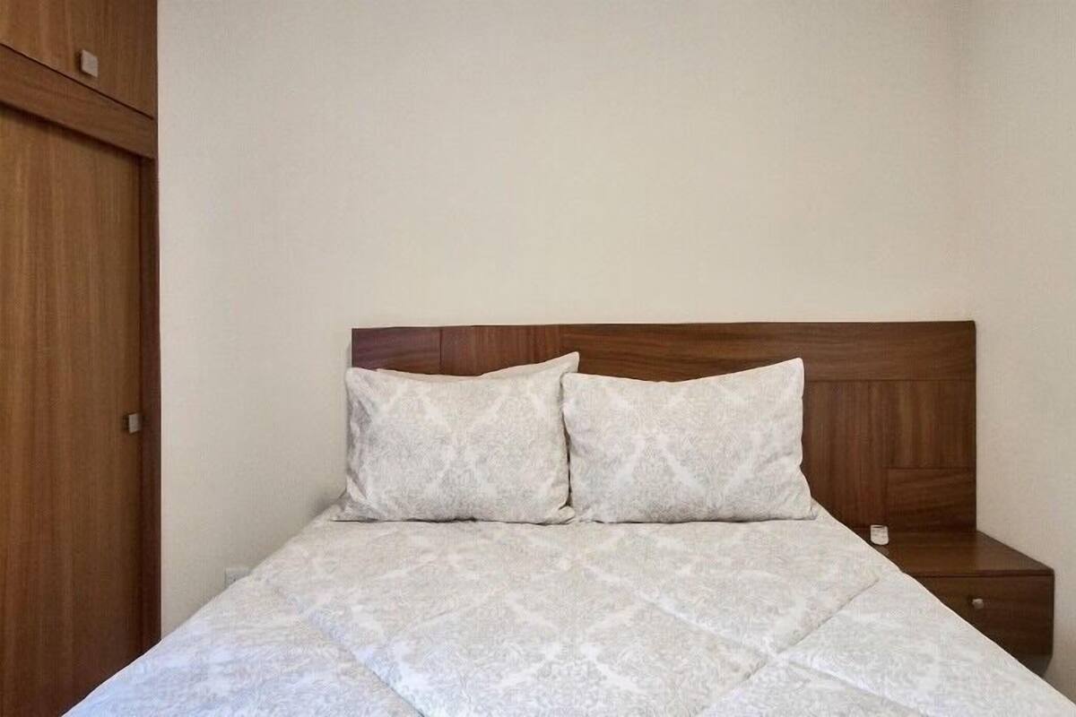 A neatly made bed with a quilted cover and two pillows, a wooden headboard, and a small bedside table with a lamp.
