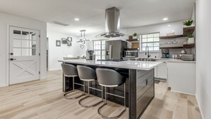 A modern kitchen with a central island, bar stools, a microwave, and a coffee machine. - Chic OKC Retreat Near Lake Hefner -Family Friendly (Oklahoma City)