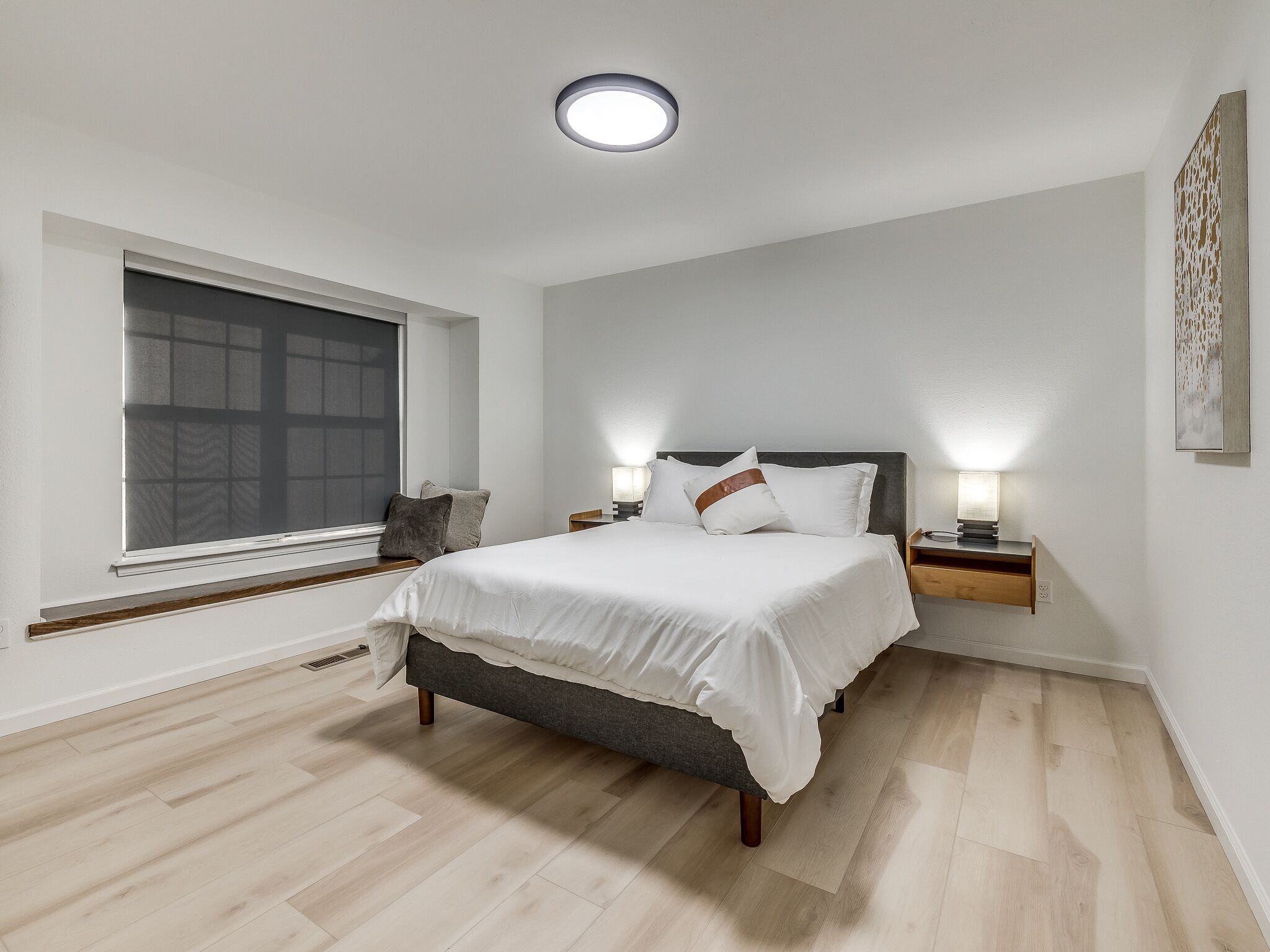 Une chambre à coucher avec un lit, des tables de chevet, une fenêtre et un luminaire au plafond.