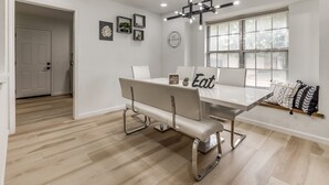 A dining area with a white table, modern chairs, a chandelier, and a window with a view. - Chic OKC Retreat Near Lake Hefner -Family Friendly (Oklahoma City)
