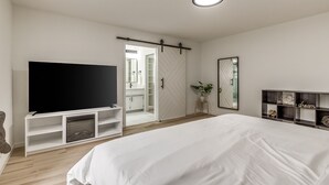 A bedroom with a large bed, a TV, a wardrobe, a mirror, and a shelf with decorative items. - Chic OKC Retreat Near Lake Hefner -Family Friendly (Oklahoma City)