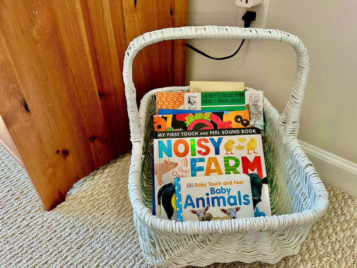 Un panier en osier blanc rempli de livres pour enfants, posé sur un tapis.