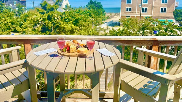 Une terrasse en bois avec une table dressée pour un repas, donnant sur un quartier résidentiel avec des maisons et un ciel dégagé.