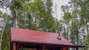 Une cabane avec un toit recouvert de tuiles rouges, un revêtement extérieur en bois et une véranda avec des chaises rouges.