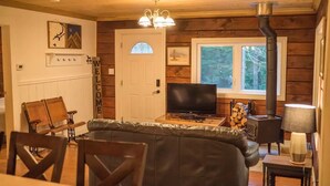 L’intérieur chaleureux d’un chalet, avec un décor en bois, un téléviseur, une cheminée et un banc.