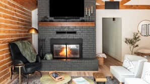 Una sala moderna con chimenea, televisor de pantalla plana montado encima y un rincón de estar acogedor con una butaca y un sofá.