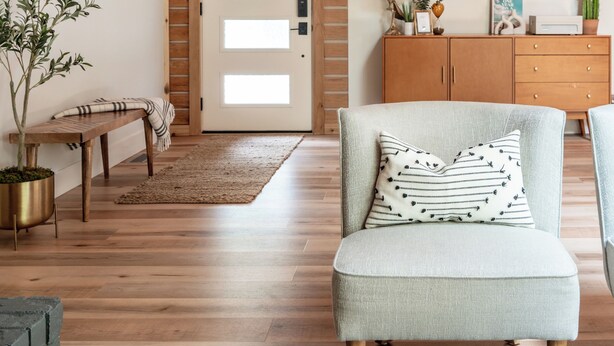 Una sala de estar moderna con techo de madera, un banco, un sillón acolchado, un pequeño otoman, un armario de madera y una puerta con paneles de vidrio esmerilado.