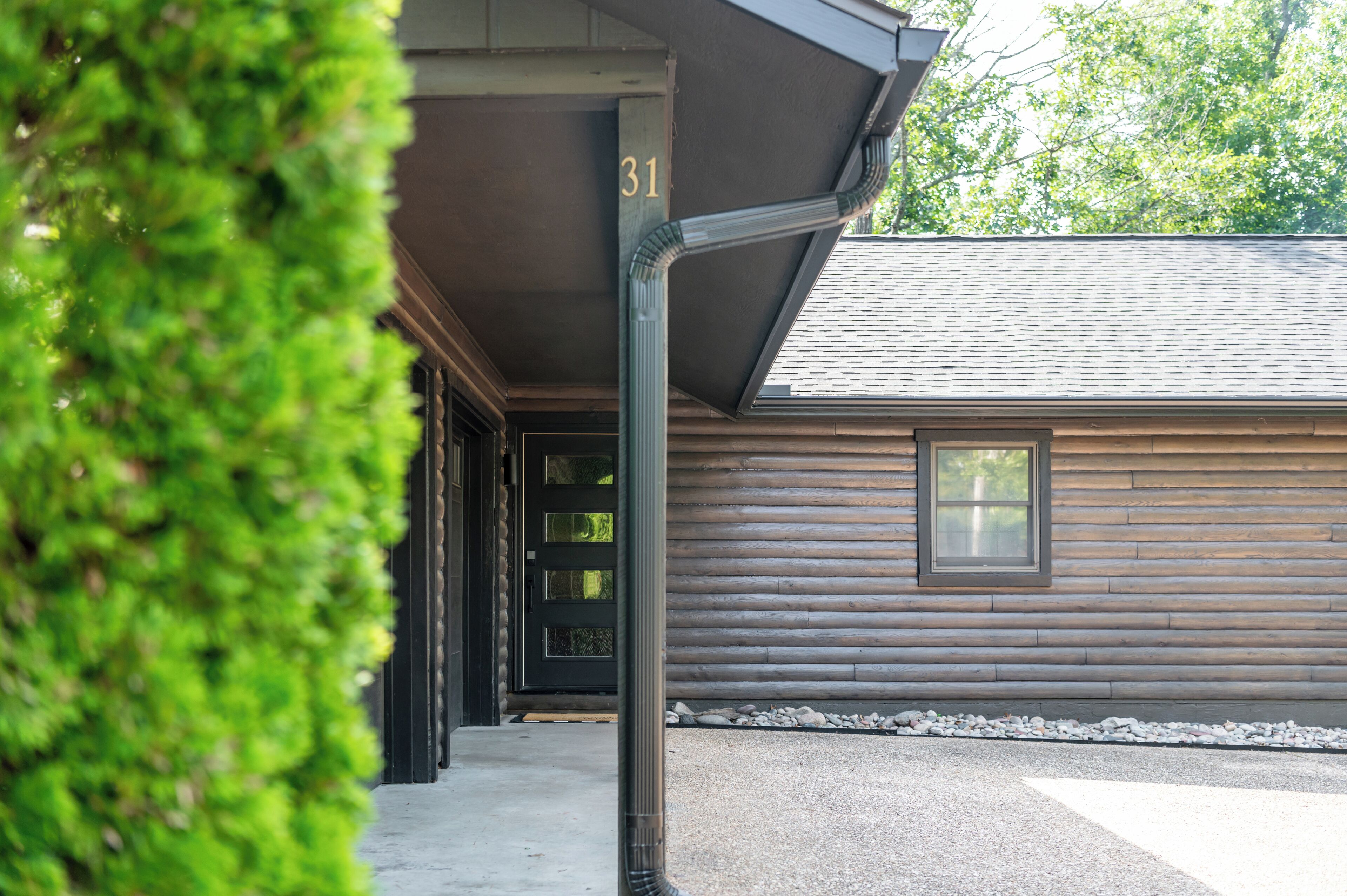 A log cabin with a black door and a window, number 31, and a gravel path leading to it.