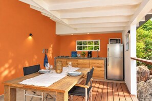 An outdoor kitchen area with a wooden table, chairs, and a built-in microwave.