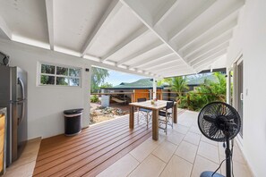 A covered patio area with a table and chairs, a fan, and a trash can.