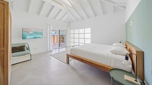 A modern bedroom with a large bed, a desk, and a view of the outdoors.