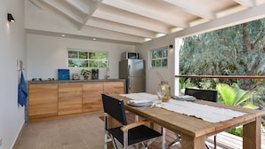 A modern kitchen with wooden cabinets, a stainless steel refrigerator, and a dining area with a wooden table and chairs.