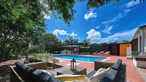 A poolside area with lounge chairs, a covered seating area, and a clear blue sky.