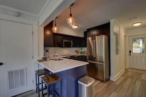 A modern kitchen with dark cabinets, stainless steel appliances, a white island with stools, and pendant lighting.