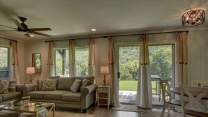 A living room with a sofa, coffee table, and a dining table with chairs. There is a window with curtains and a view of greenery outside. - Golden Bear- lovely one bedroom with fireplace (Sky Valley)