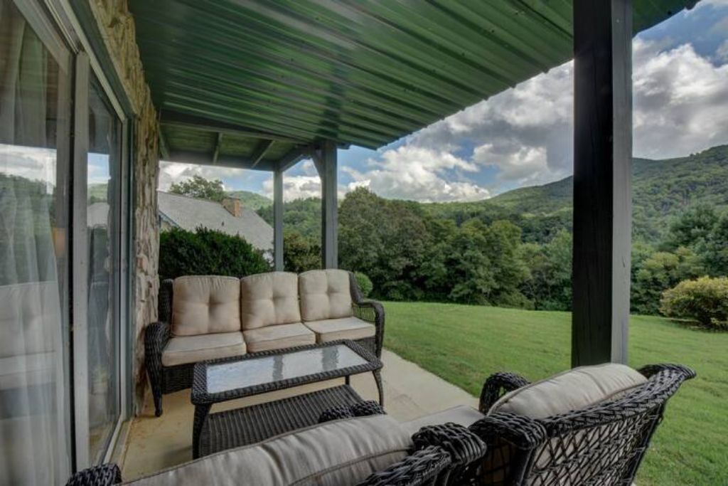 A covered outdoor seating area with a sofa and chairs, overlooking a lush green landscape and hills.