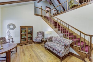 Un salón espacioso con una escalera de madera, un sofá estampado, un aparador de madera y una estatua.