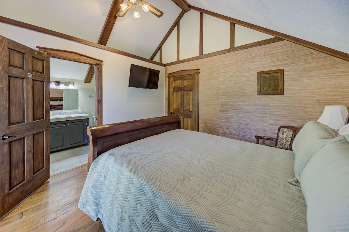 Un dormitorio con una cama grande, vigas de techo de madera, una puerta de madera, una mesita y una silla.