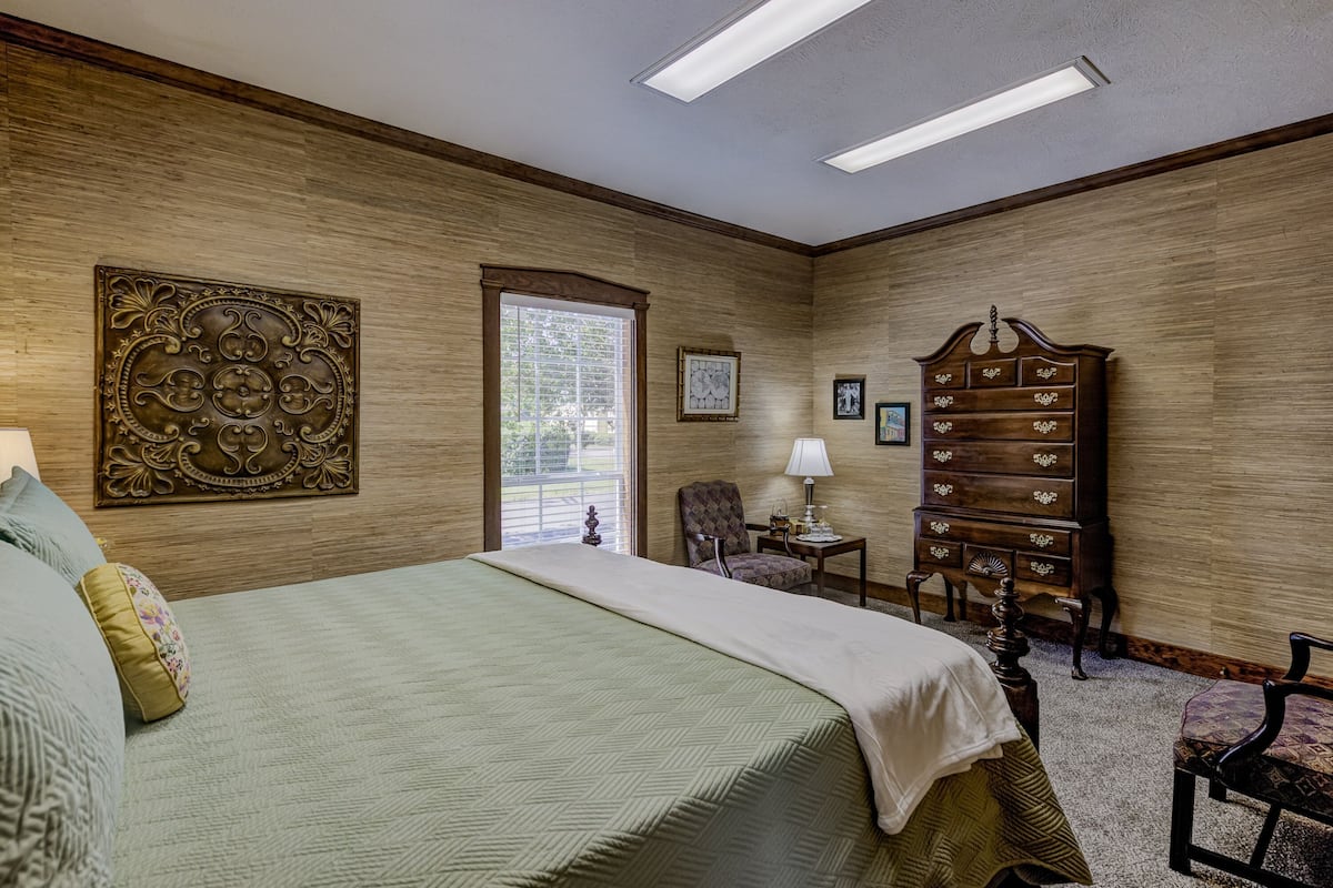 Un dormitorio con una cama grande, un aparador, una silla y una ventana con persianas.