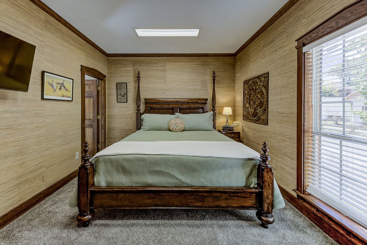 Un dormitorio con cama con dosel, una mesita de noche con lámpara y una ventana con persianas.
