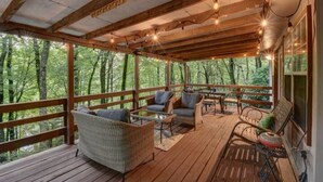 Um deck de madeira com móveis de exterior, janelas amplas e vista para árvores.