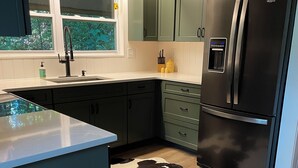 Uma cozinha moderna com armários verde escuro, uma geladeira de aço inoxidável e um tapete de couro de vaca.