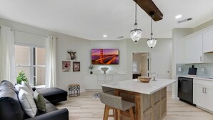 Una cocina moderna con armarios blancos, una isla central y una zona de comedor con sofá negro y taburetes de bar.