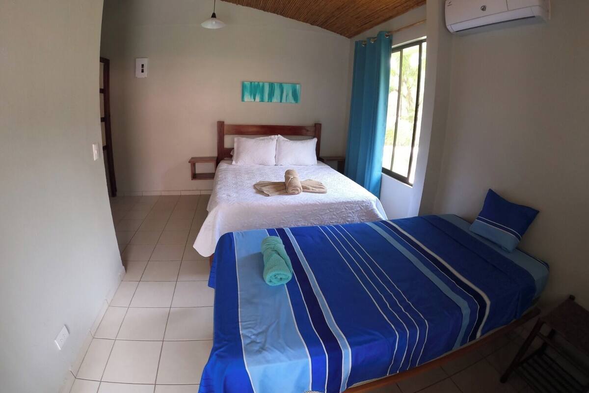 Een kamer met een bed, een klein bed, een plafondventilator, een airconditioning en een raam met gordijnen.