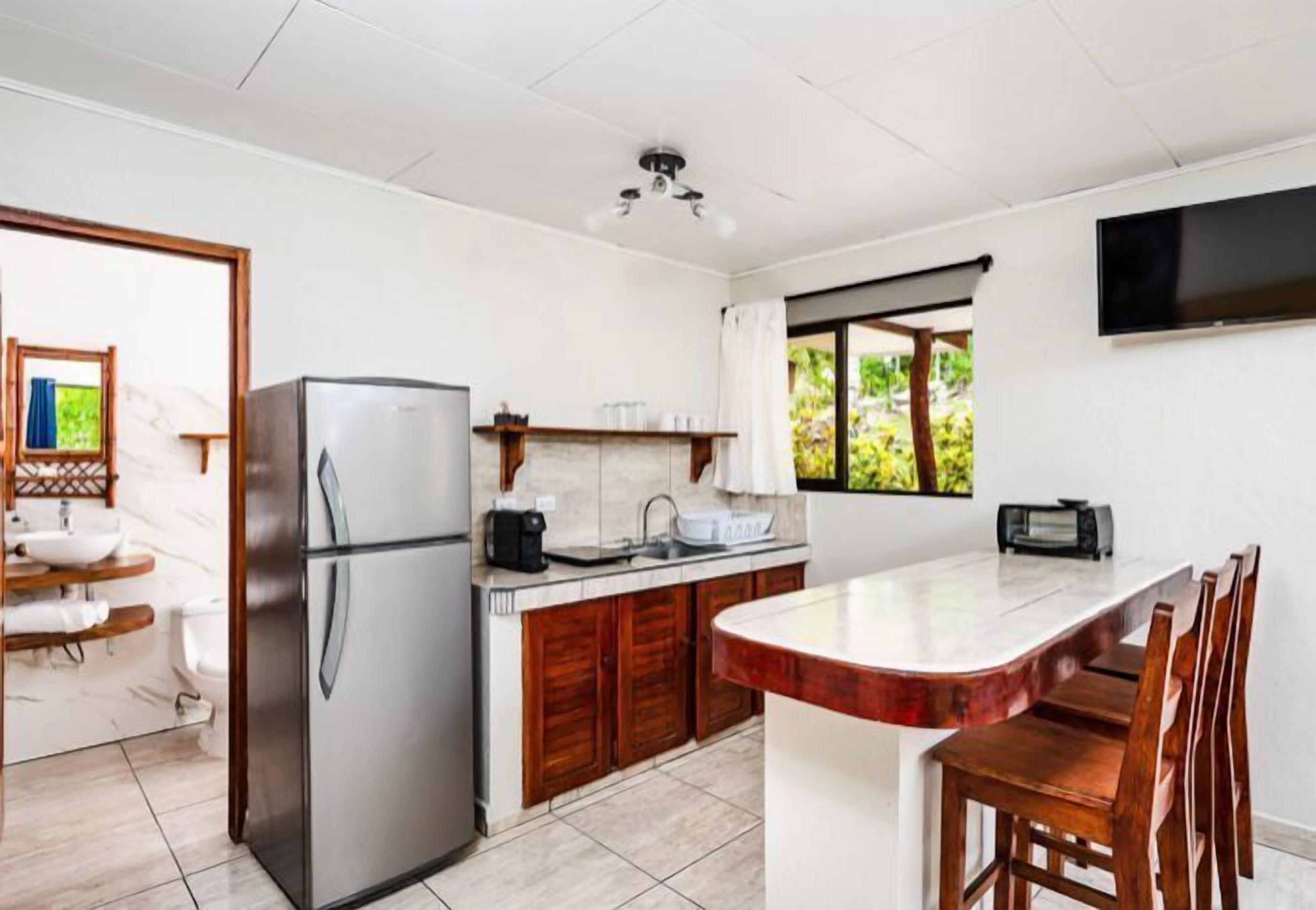 A modern kitchen with a stainless steel refrigerator, wooden cabinets, a marble countertop, and a large island with bar stools.