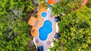 En vy från ovan av ett semesterområde med en stor swimmingpool, solstolar och omgivet av frodig grönska.
