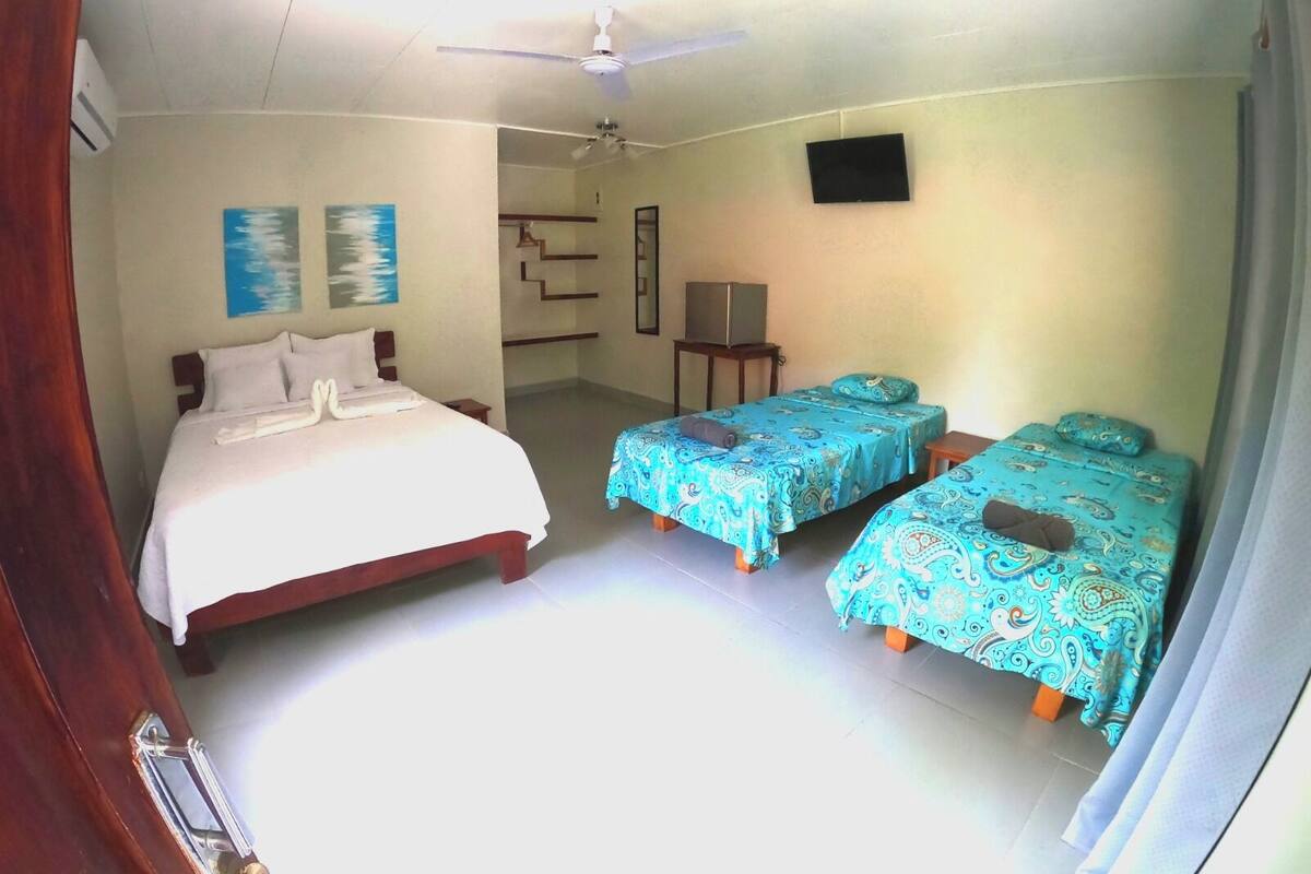 Een hotelkamer met een groot bed, twee kleinere bedden, een plafondventilator en een televisie.