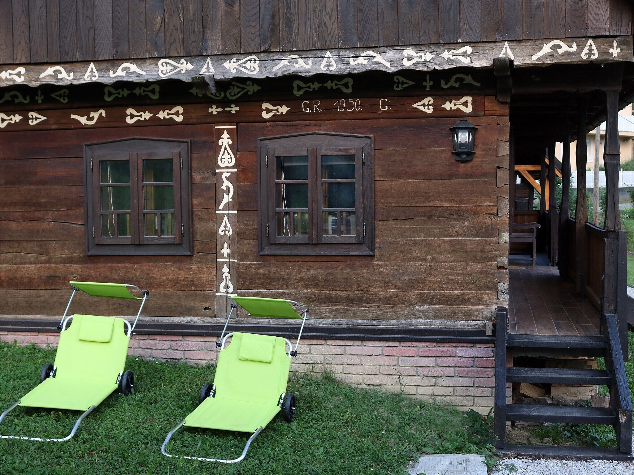 A wooden building with two windows and a door, a green chair, and a small outdoor area with grass.