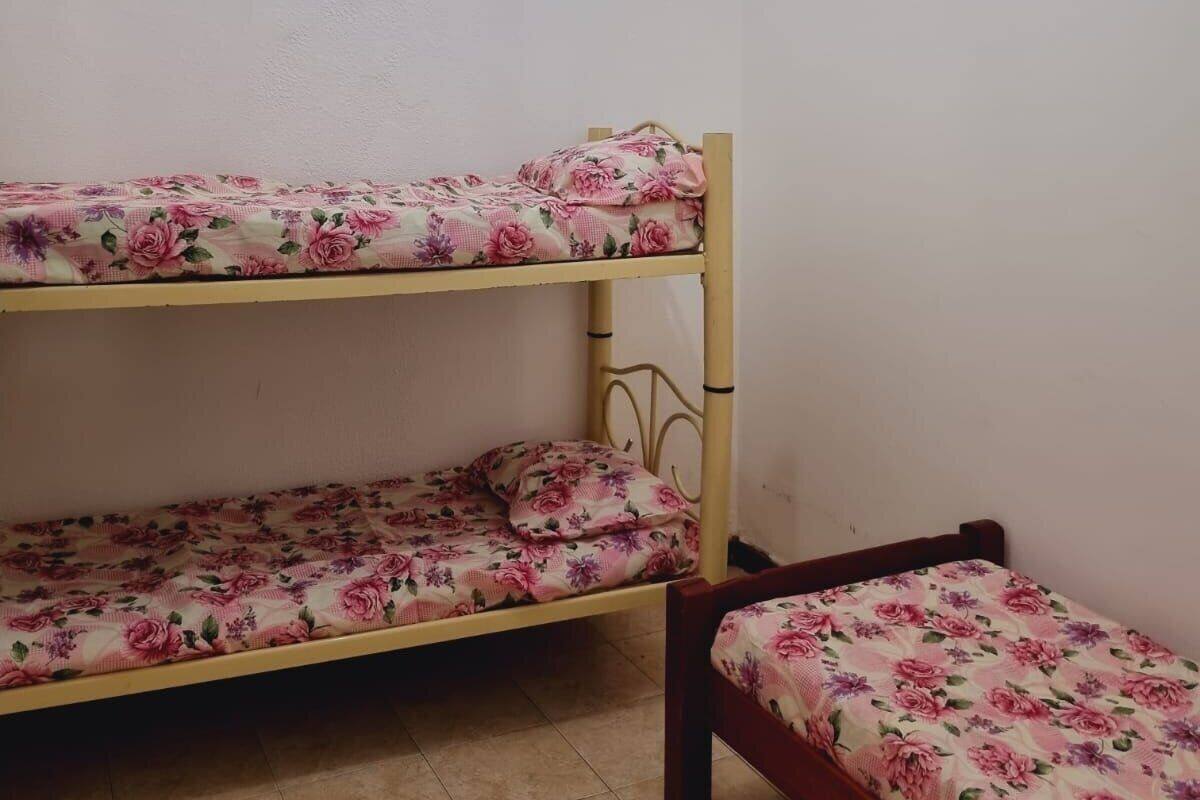 Una cama litera con ropa de cama floral en una habitación con paredes lisas y suelo de baldosas.