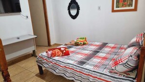 Un dormitorio con cama, televisor montado en la pared, espejo y un cuadro enmarcado.